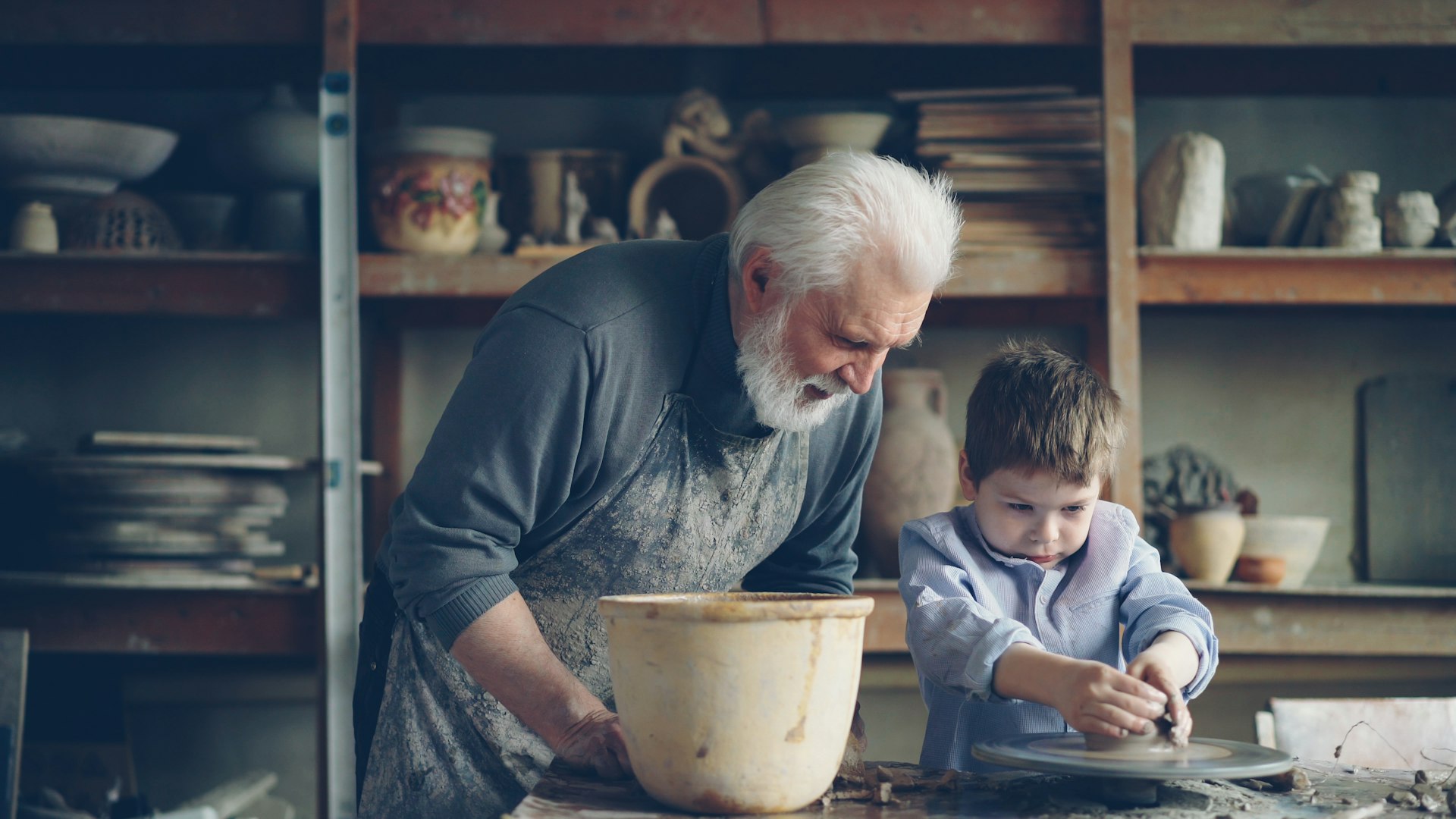 A grandfather teaches a boy pottery.
